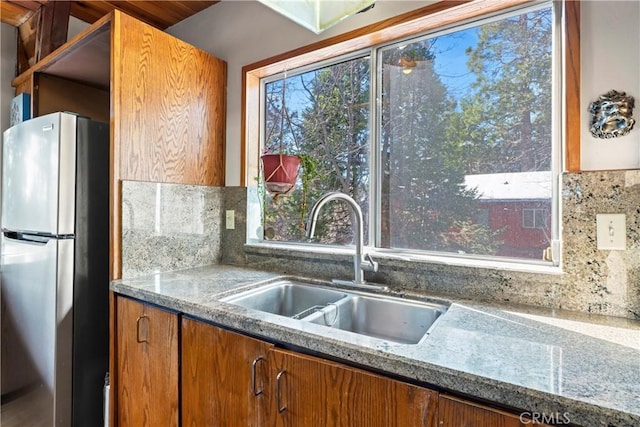 26509 Lake Forest Dr, Twin Peaks, CA 92391 - kitchen with light stone counters, brown cabinets, a sink, freestanding refrigerator, and backsplash