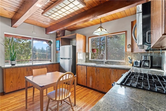 kitchen featuring backsplash, light wood-style flooring, brown cabinetry, stainless steel appliances, and a sink