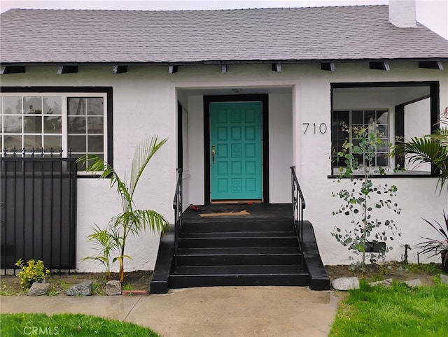 property entrance with stucco siding and a shingled roof