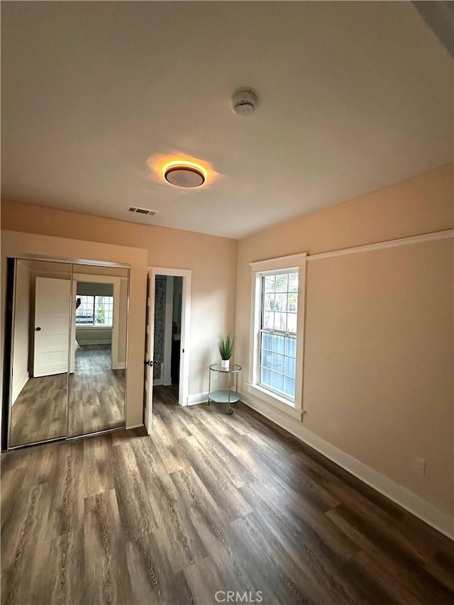 unfurnished bedroom with dark wood-style floors, visible vents, and baseboards