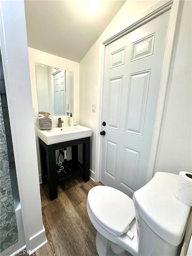 bathroom featuring toilet, a sink, wood finished floors, baseboards, and vaulted ceiling