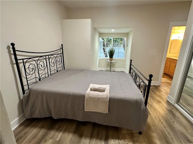 bedroom featuring wood finished floors, baseboards, and ensuite bathroom