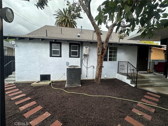 rear view of house with a shingled roof, central air condition unit, and stucco siding