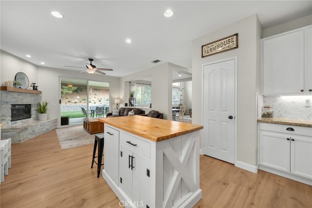 kitchen with open floor plan, a stone fireplace, white cabinets, light wood finished floors, and wooden counters