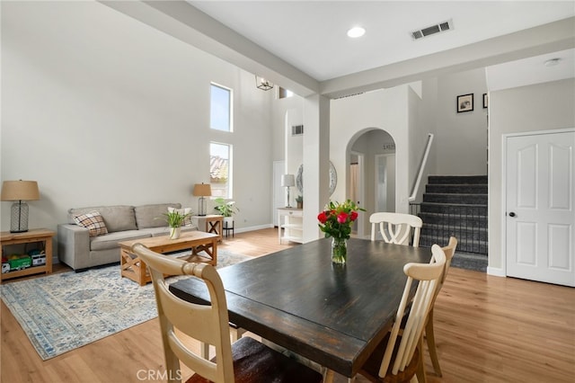 dining space featuring visible vents, light wood-style flooring, stairway, arched walkways, and baseboards