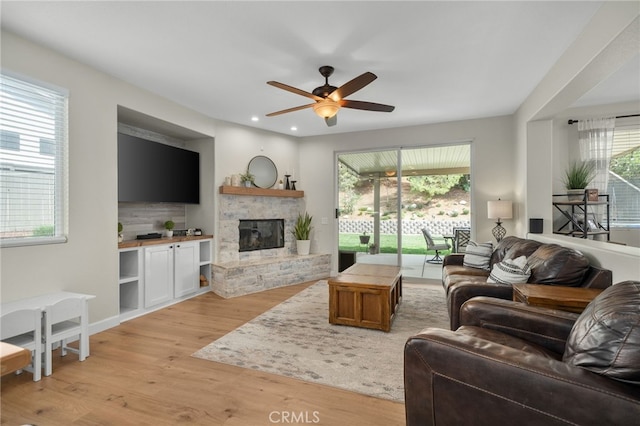 living room with a stone fireplace, recessed lighting, light wood-type flooring, and ceiling fan