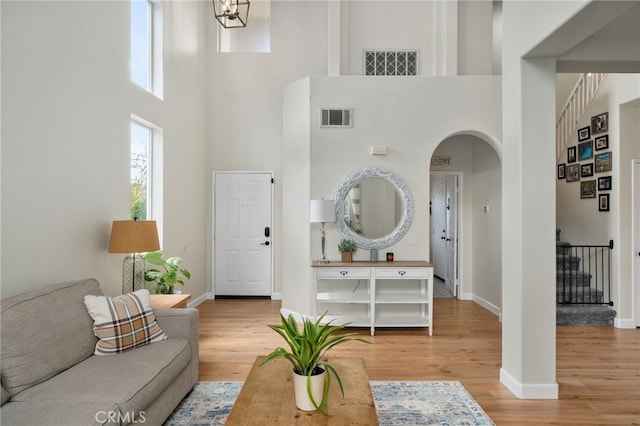 living area with stairway, wood finished floors, visible vents, baseboards, and arched walkways