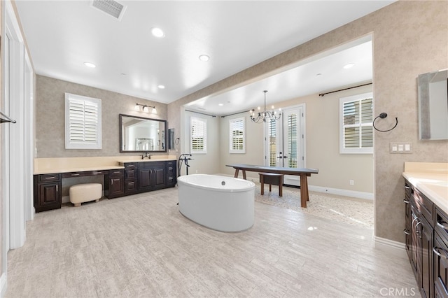 bathroom featuring baseboards, visible vents, a soaking tub, two vanities, and a sink