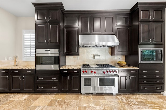 kitchen with backsplash, light stone countertops, under cabinet range hood, appliances with stainless steel finishes, and stone finish floor