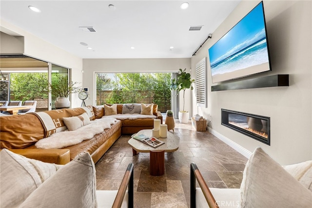 living area with recessed lighting, visible vents, stone tile floors, and a glass covered fireplace