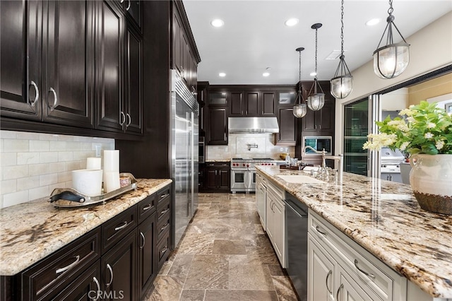 kitchen with recessed lighting, a sink, under cabinet range hood, decorative light fixtures, and high quality appliances