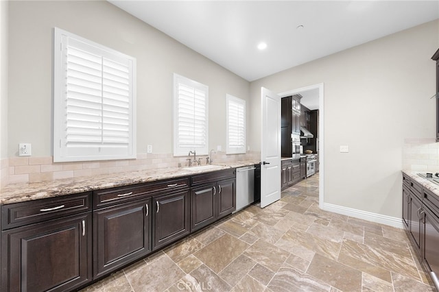 kitchen with baseboards, a sink, stone finish floor, dishwasher, and tasteful backsplash