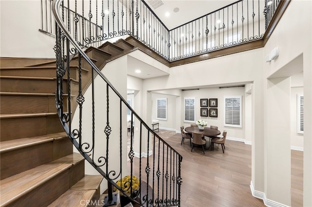 stairs with recessed lighting, a high ceiling, baseboards, and wood finished floors