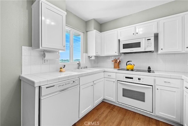 kitchen with white cabinetry, white appliances, tile counters, and a sink