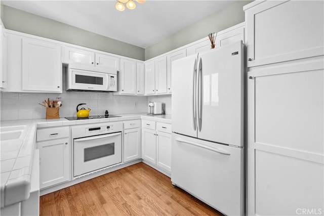 kitchen with backsplash, white cabinetry, tile countertops, white appliances, and light wood-style floors