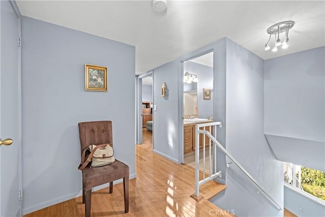 hall featuring an upstairs landing, light wood-type flooring, and baseboards