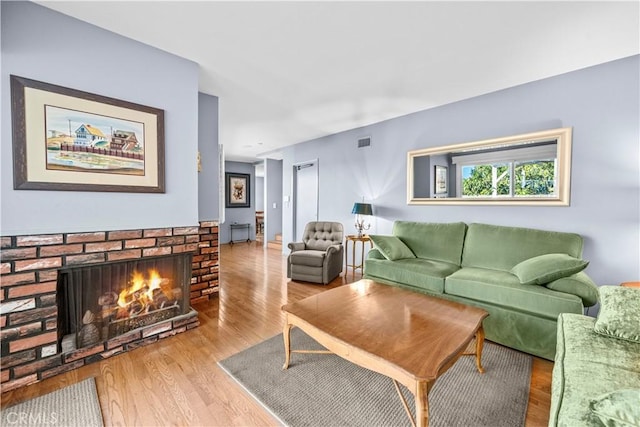 living area featuring a brick fireplace, wood finished floors, and visible vents