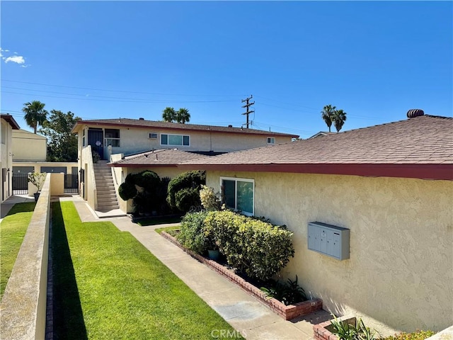 exterior space featuring a shingled roof, fence, stairway, stucco siding, and a lawn