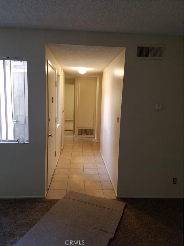 hall with light tile patterned floors, visible vents, and a textured ceiling