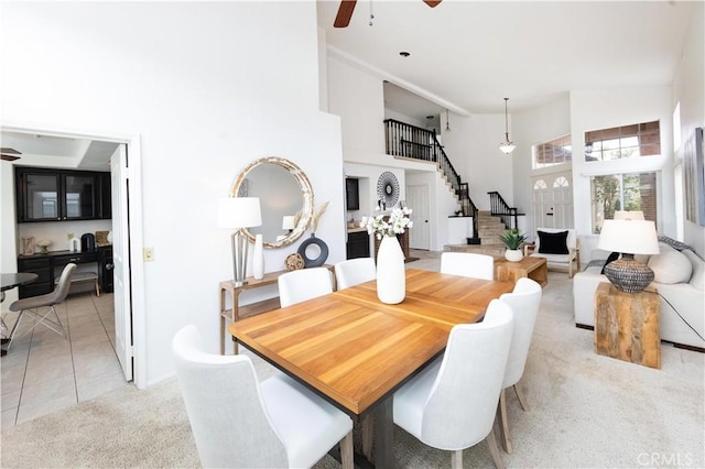 dining space with stairway, light carpet, a high ceiling, light tile patterned flooring, and a ceiling fan