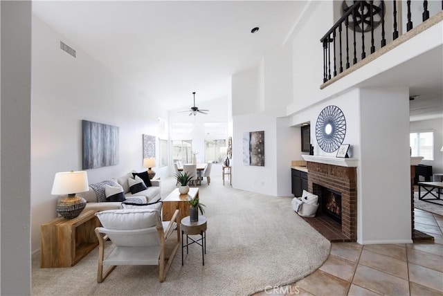 living area with visible vents, a brick fireplace, high vaulted ceiling, and ceiling fan