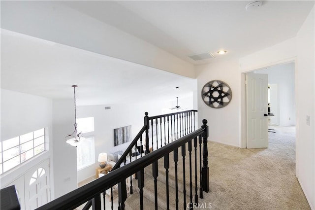 corridor with a notable chandelier, an upstairs landing, and light colored carpet