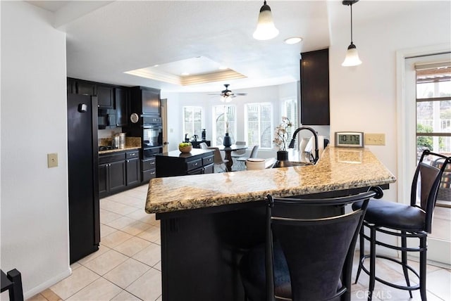 kitchen featuring a kitchen bar, a sink, a tray ceiling, freestanding refrigerator, and a peninsula