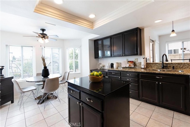 kitchen with dark stone countertops, light tile patterned floors, a tray ceiling, a sink, and dark cabinets