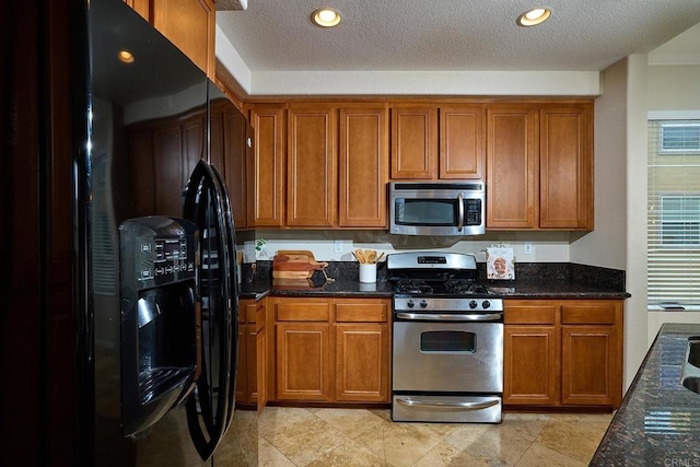 kitchen with a textured ceiling, dark stone countertops, brown cabinets, and stainless steel appliances