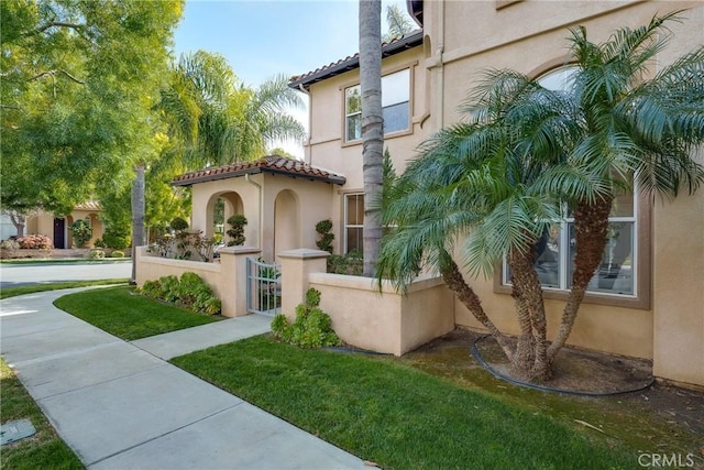 exterior space featuring a tiled roof, a gate, a fenced front yard, and stucco siding