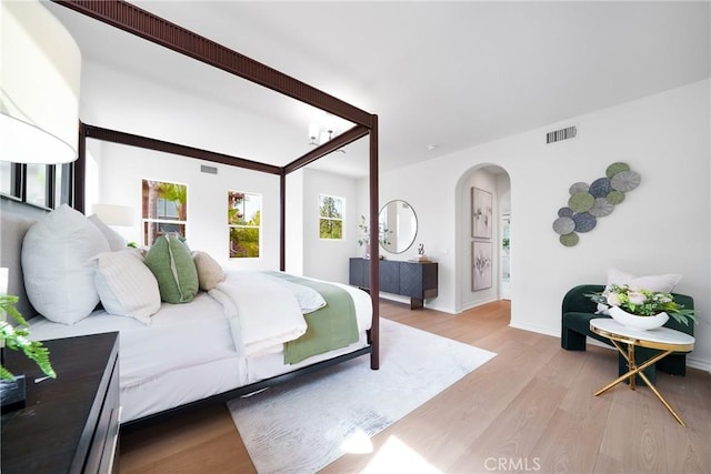 bedroom featuring baseboards, wood finished floors, visible vents, and arched walkways