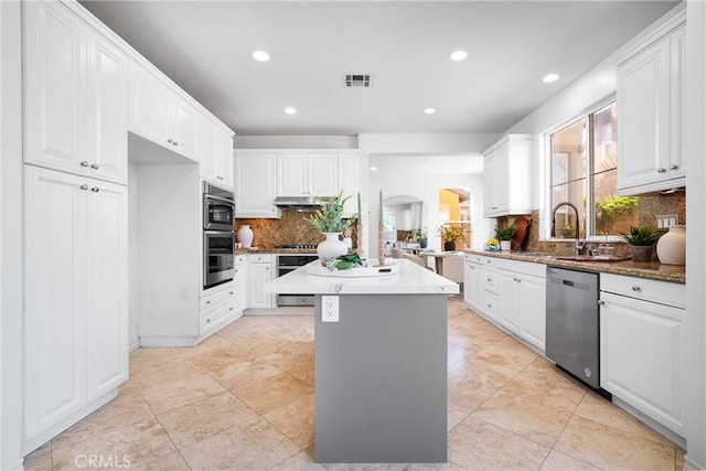 kitchen featuring visible vents, under cabinet range hood, a center island, stainless steel appliances, and arched walkways