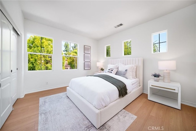 bedroom with light wood finished floors, visible vents, and baseboards