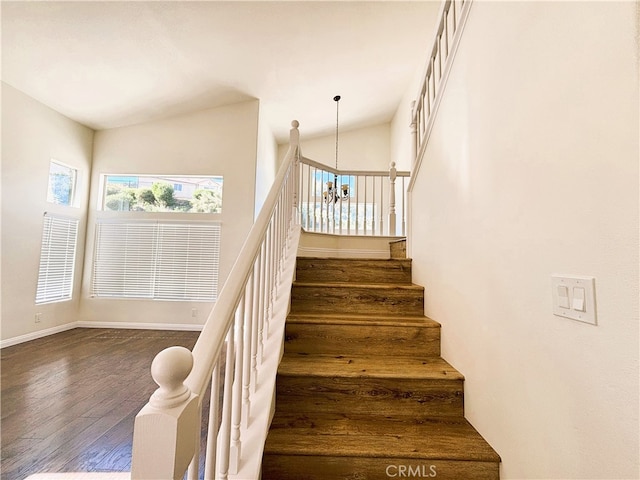 stairs featuring baseboards, lofted ceiling, wood finished floors, and a chandelier