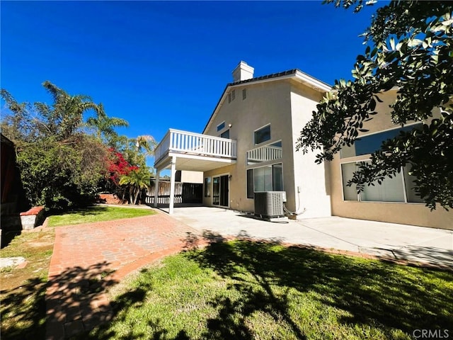 back of property with a patio, central AC unit, a chimney, stucco siding, and a lawn