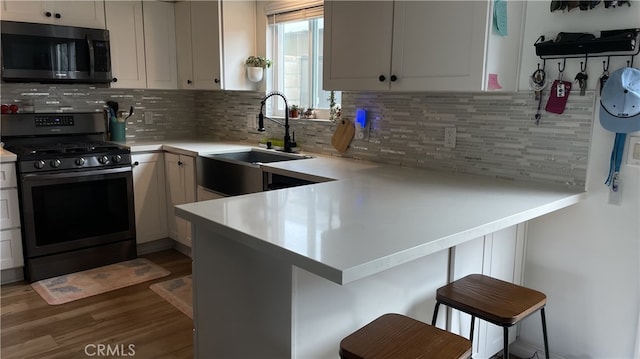 kitchen featuring stainless steel gas range oven, tasteful backsplash, light countertops, a peninsula, and a sink