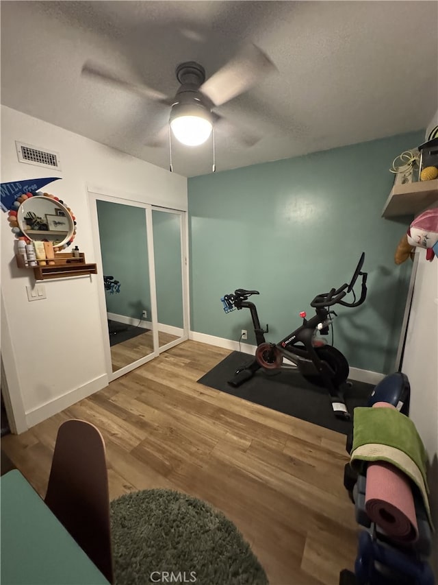 exercise area featuring visible vents, a textured ceiling, wood finished floors, baseboards, and ceiling fan