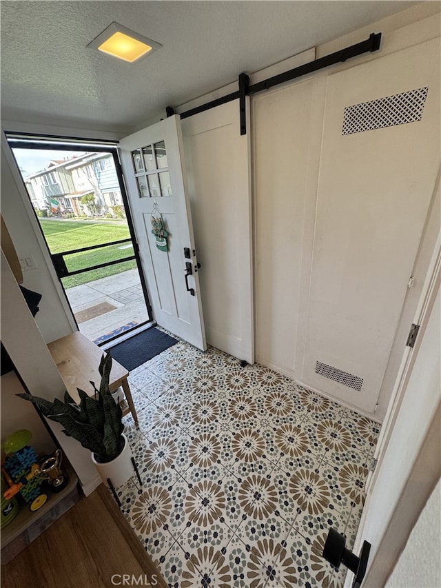 foyer featuring a barn door, light floors, and a textured ceiling