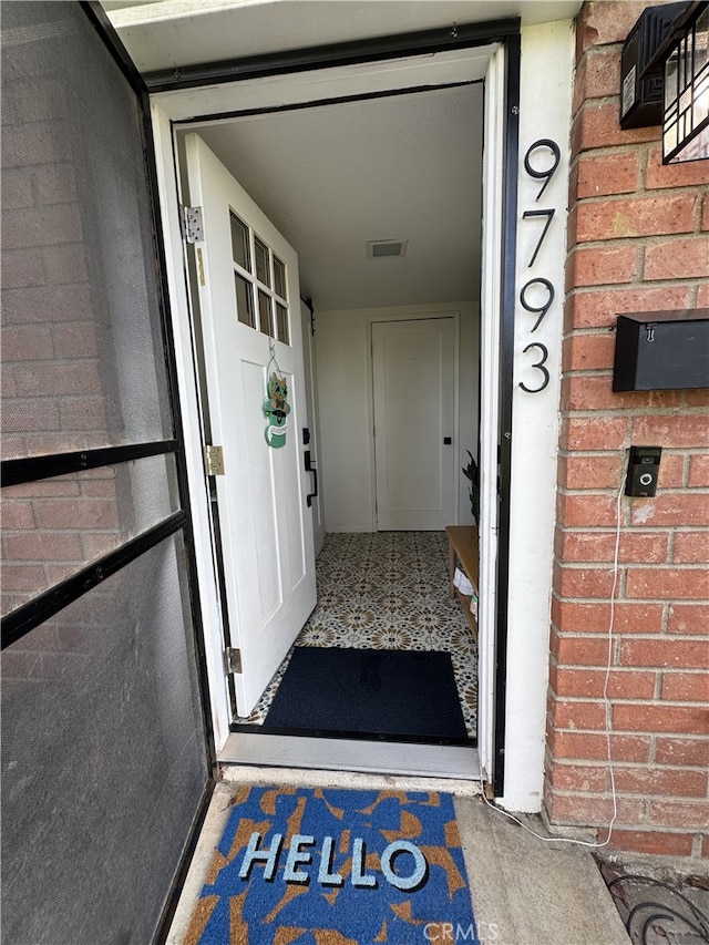 view of exterior entry featuring visible vents and brick siding