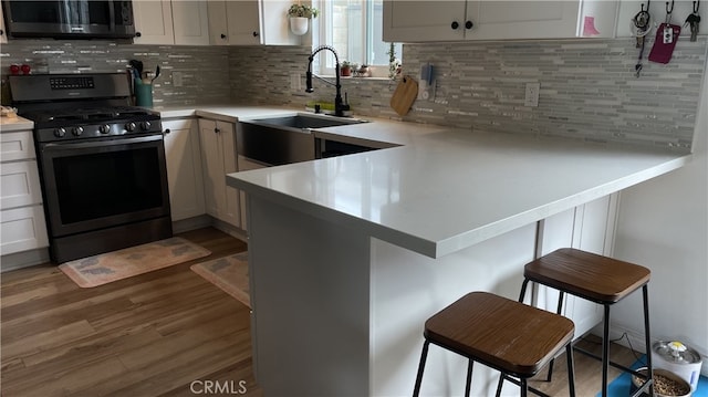 kitchen featuring wood finished floors, a peninsula, a sink, stainless steel appliances, and light countertops