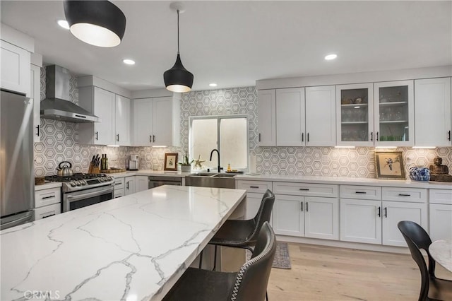 kitchen featuring light wood-style flooring, a sink, stainless steel appliances, wall chimney exhaust hood, and glass insert cabinets