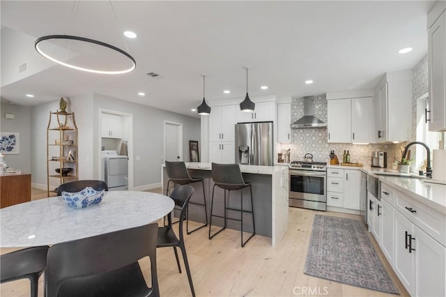 kitchen featuring washer / dryer, appliances with stainless steel finishes, white cabinets, wall chimney exhaust hood, and a sink