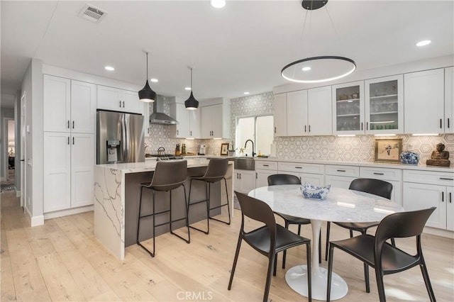 kitchen featuring wall chimney range hood, visible vents, stainless steel fridge, and light wood finished floors