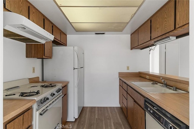 kitchen with under cabinet range hood, a sink, wood finished floors, white appliances, and light countertops