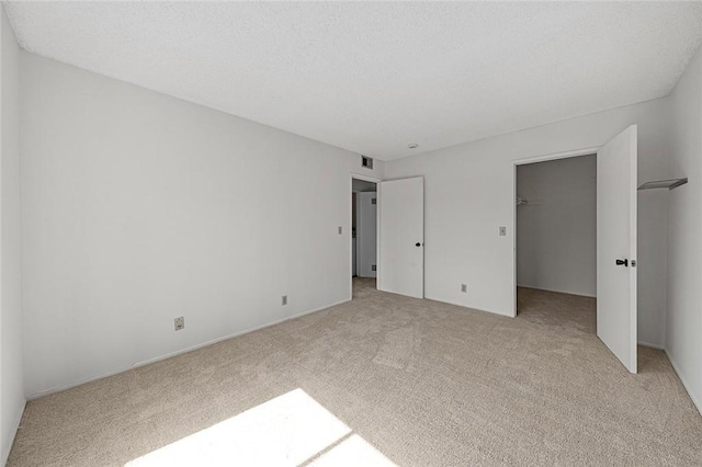 unfurnished bedroom with visible vents, a spacious closet, a closet, a textured ceiling, and light colored carpet