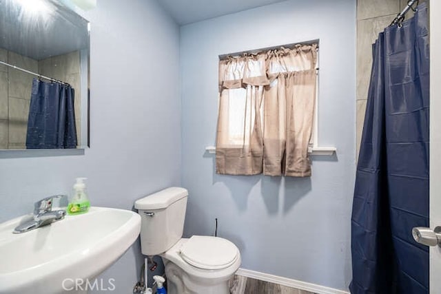 full bathroom featuring curtained shower, baseboards, toilet, wood finished floors, and a sink