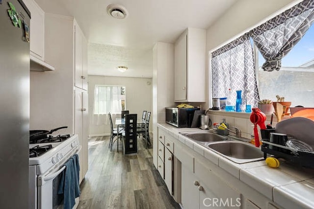 kitchen with tile countertops, white cabinets, stainless steel appliances, and wood finished floors