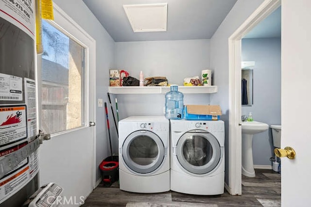 clothes washing area with gas water heater, wood finished floors, washing machine and dryer, and a sink