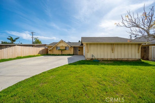 view of front of property with board and batten siding, concrete driveway, fence, and a front yard