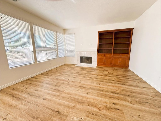 unfurnished living room featuring light wood-style flooring, built in features, a fireplace, and baseboards